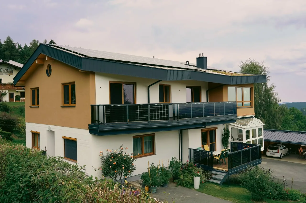Haus Anita: Ansicht des aufgestockten Hauses mit begrüntem Flachdach, PV Anlage und Balkon über dem Tal