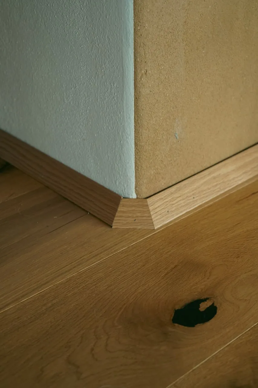 Haus Anita: Detail einer Raumecke, weiß verputzte Wand trifft auf eine Wand mit Lehmputz, darunter Eichenboden