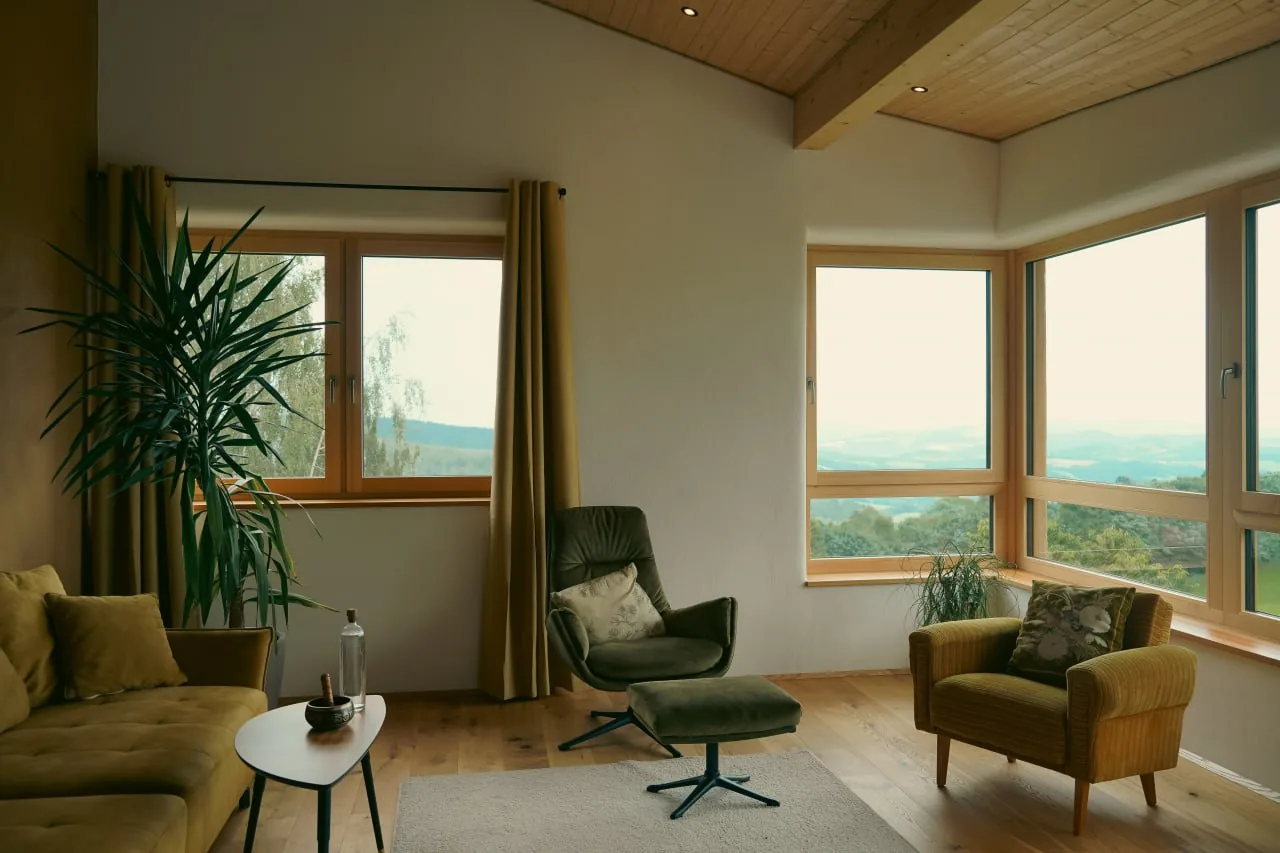 Haus Anita: Wohnraum mit Eckfenster, Holzdecke und Blick in die Hügellandschaft
