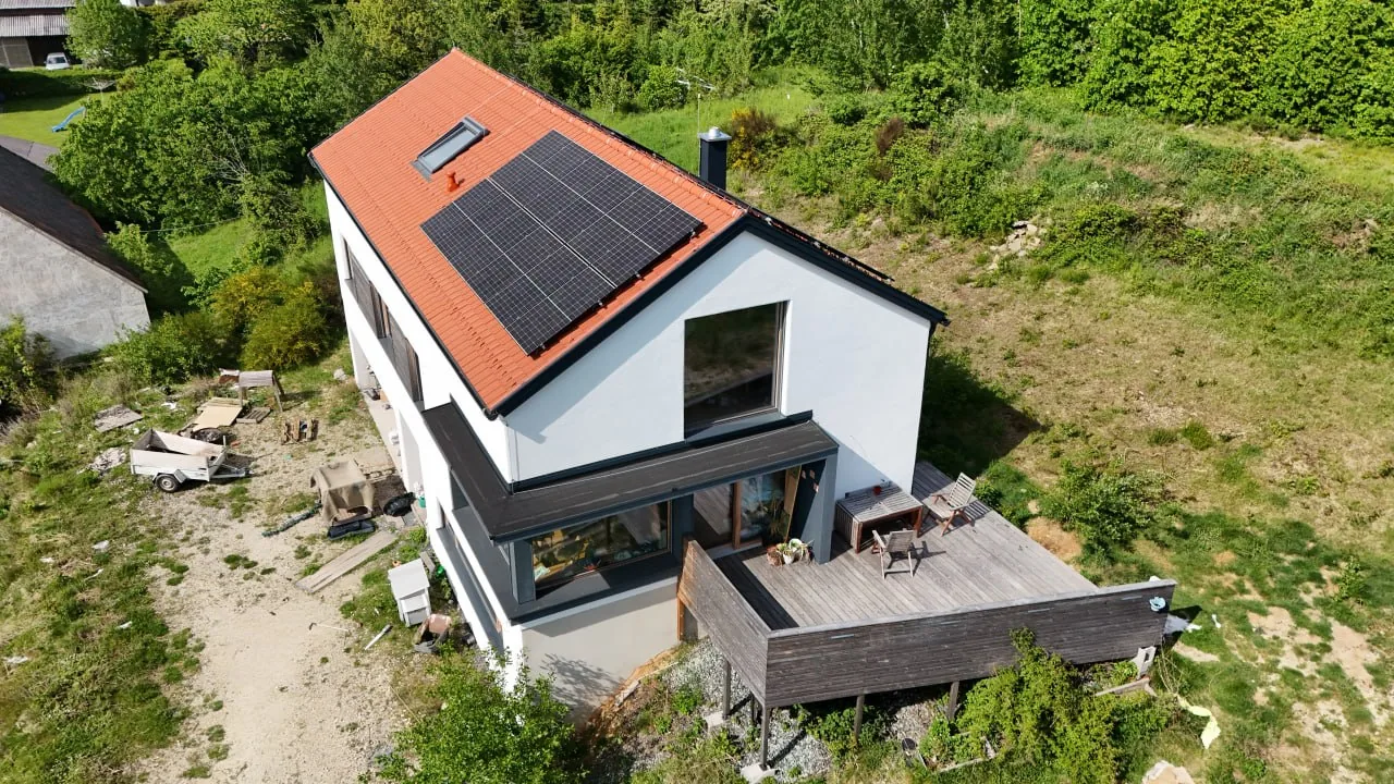 Haus Antonia: weißes Wohnhaus mit rotem Ziegeldach, Photovoltaik und Holzterrasse am Hang, Luftbild