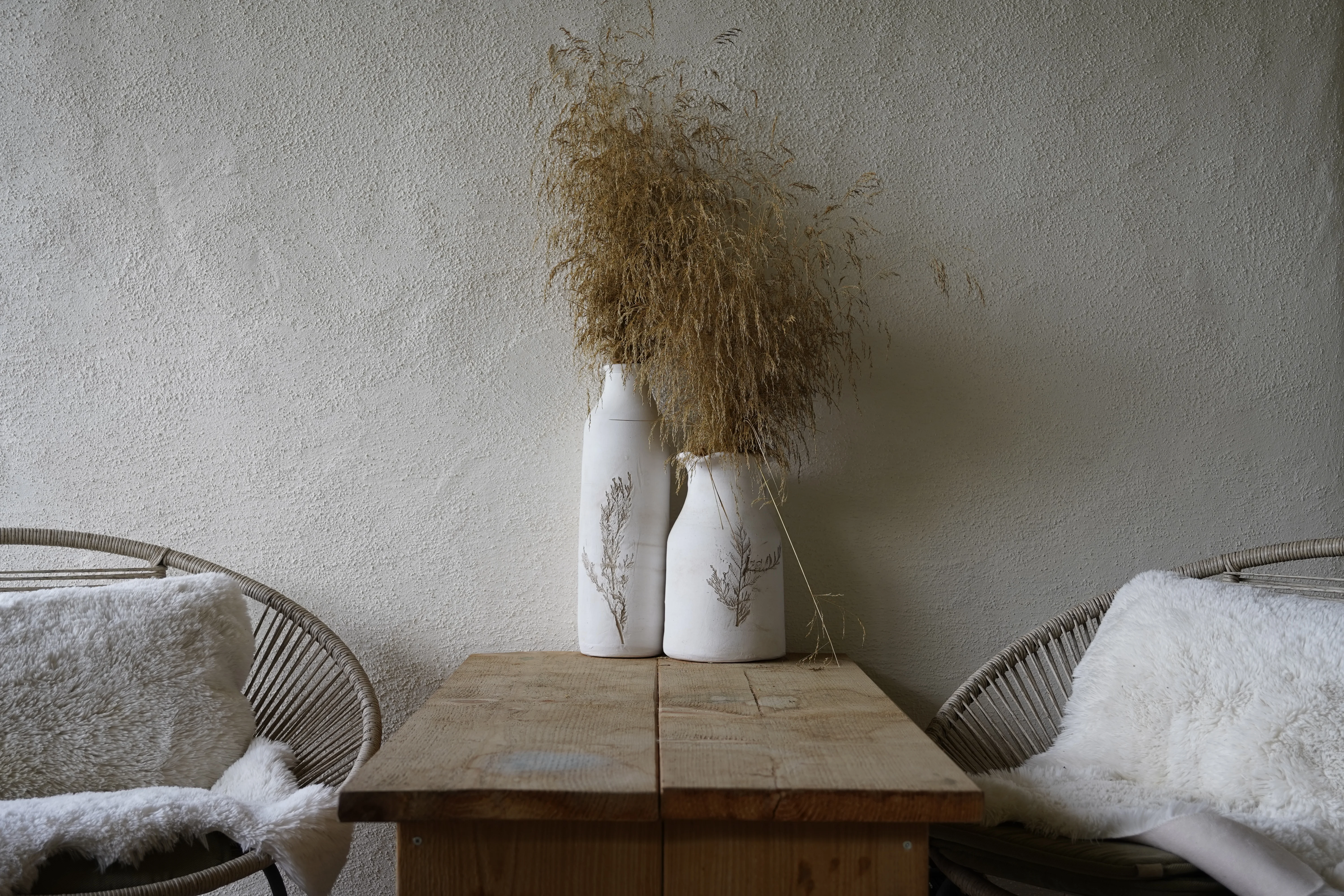 Haus Renate: Naturputzwand mit weißen Keramikvasen und Trockenblumen
