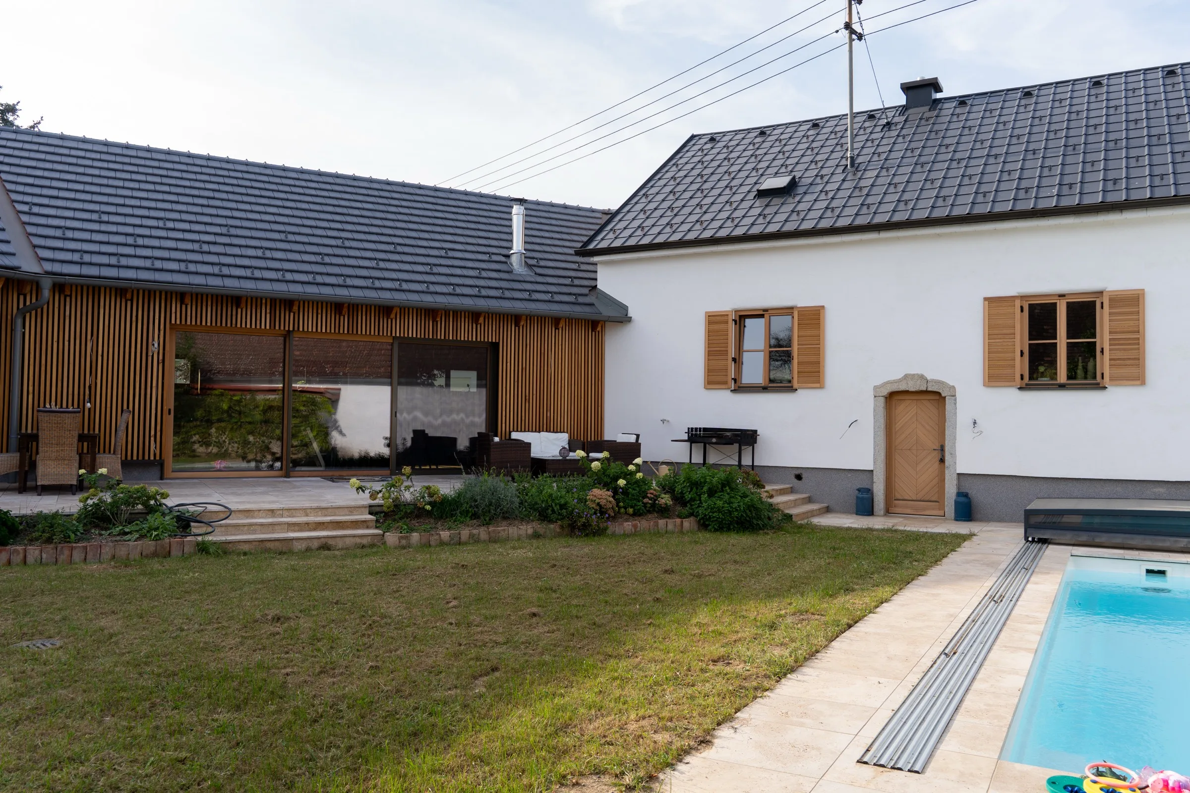 Haus Teresa: Innenhof mit sanierter weißer Fassade des Altbaus und neuem Holz-Zubau, Pool im Vordergrund