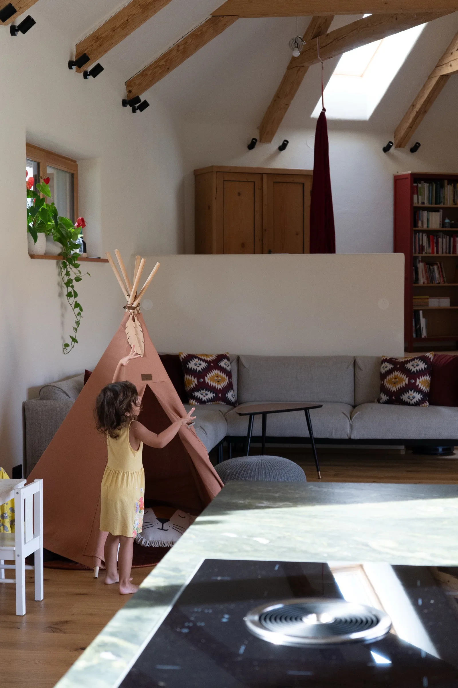 Haus Teresa: Kind spielt im Wohnraum unter freigelegter Holzbalkenkonstruktion mit Dachfenster