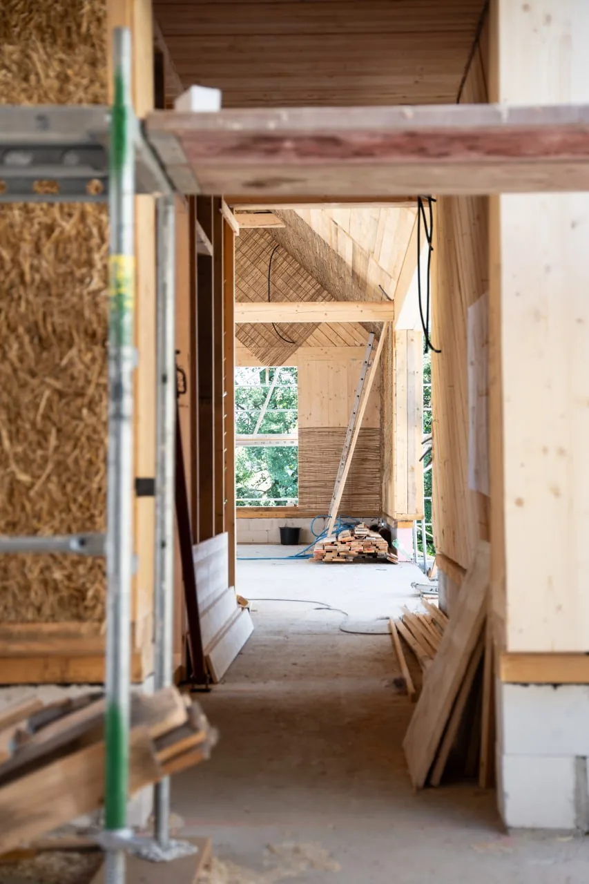 Projekt Lauber: Innenraum im Rohbau, Durchgang zwischen Wänden mit sichtbaren Strohballen und Holzkonstruktion
