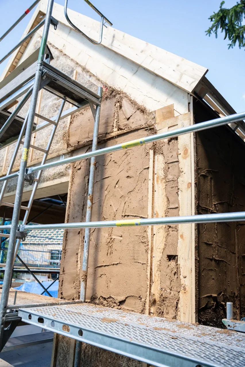 Projekt Lauber: Wandaufbau im Rohbau, Strohballen zwischen den Holzständern mit erstem Lehmbewurf, davor das Gerüst