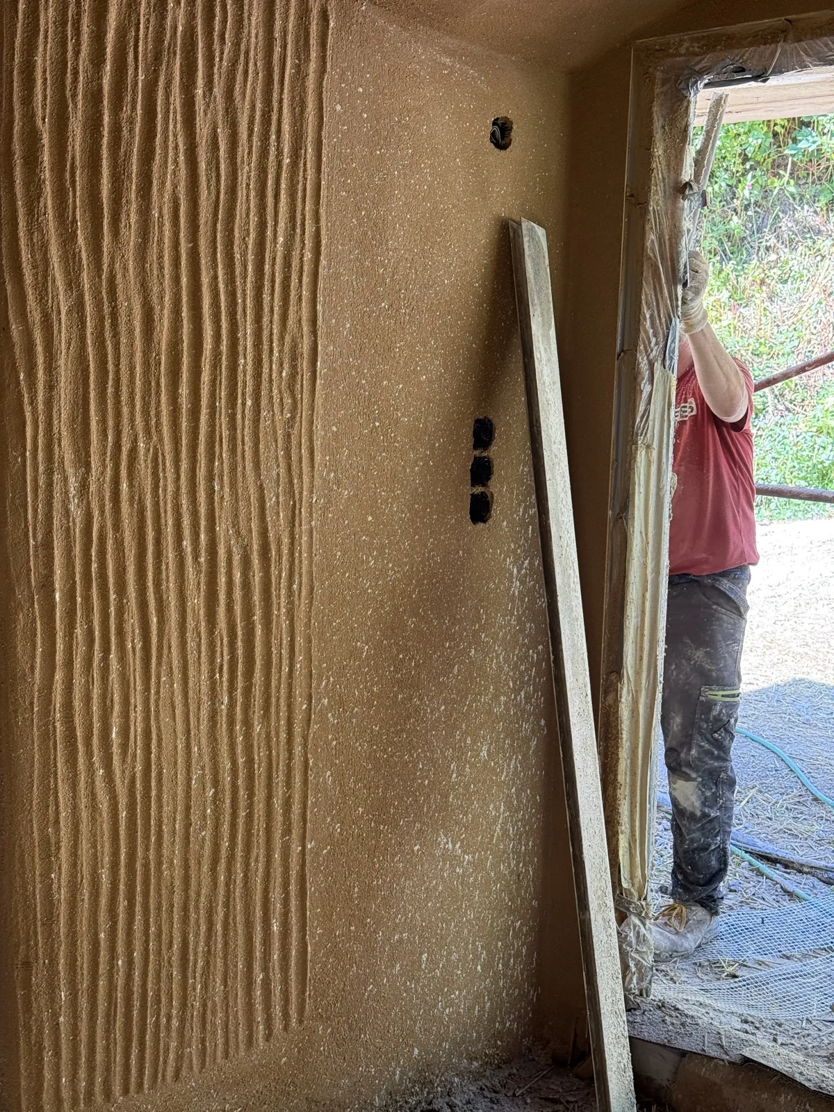 Innenwand mit Lehmputz, in den von Hand eine feine senkrechte Kammstruktur gezogen wurde