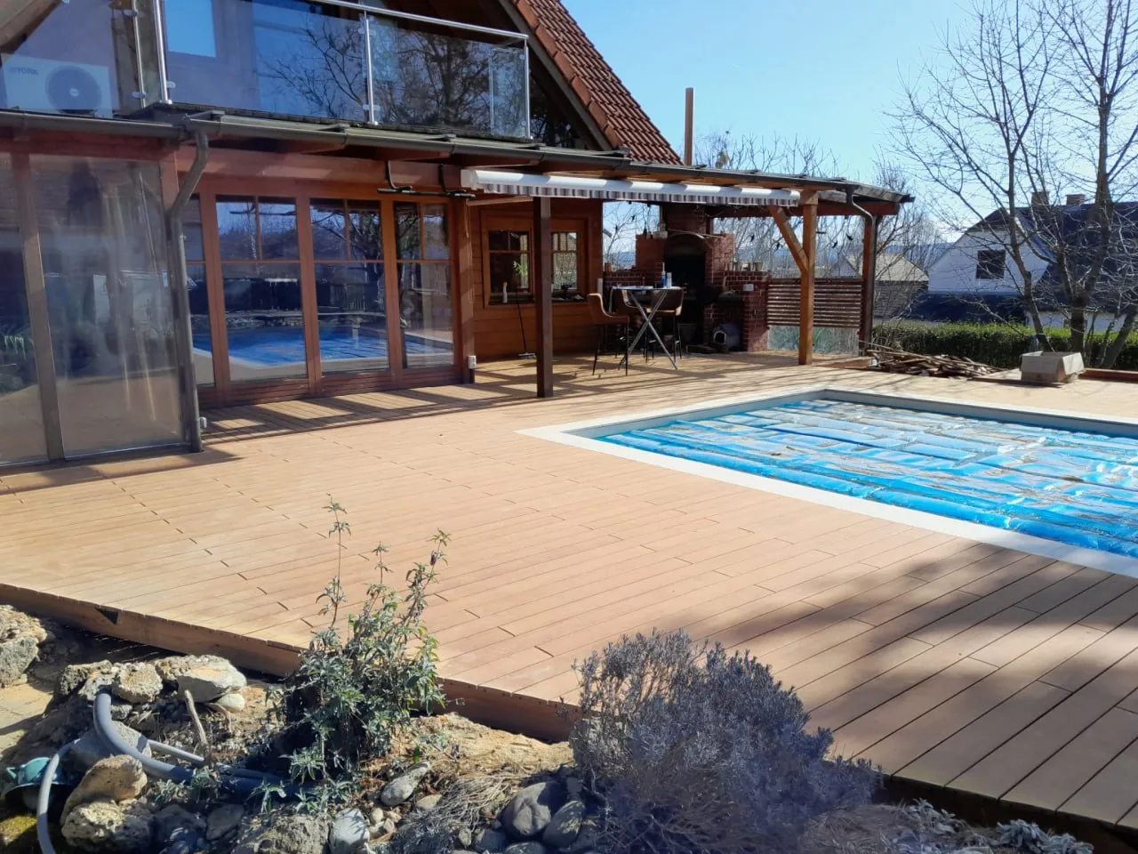 Holzterrasse vor einem Wohnhaus mit Glasfront, im Vordergrund der Pool