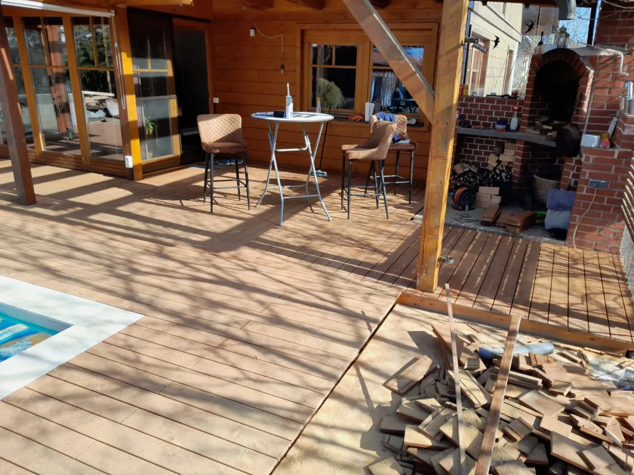 Überdachter Sitzbereich auf der Holzterrasse mit Stehtisch und Barhockern neben dem Holzhaus