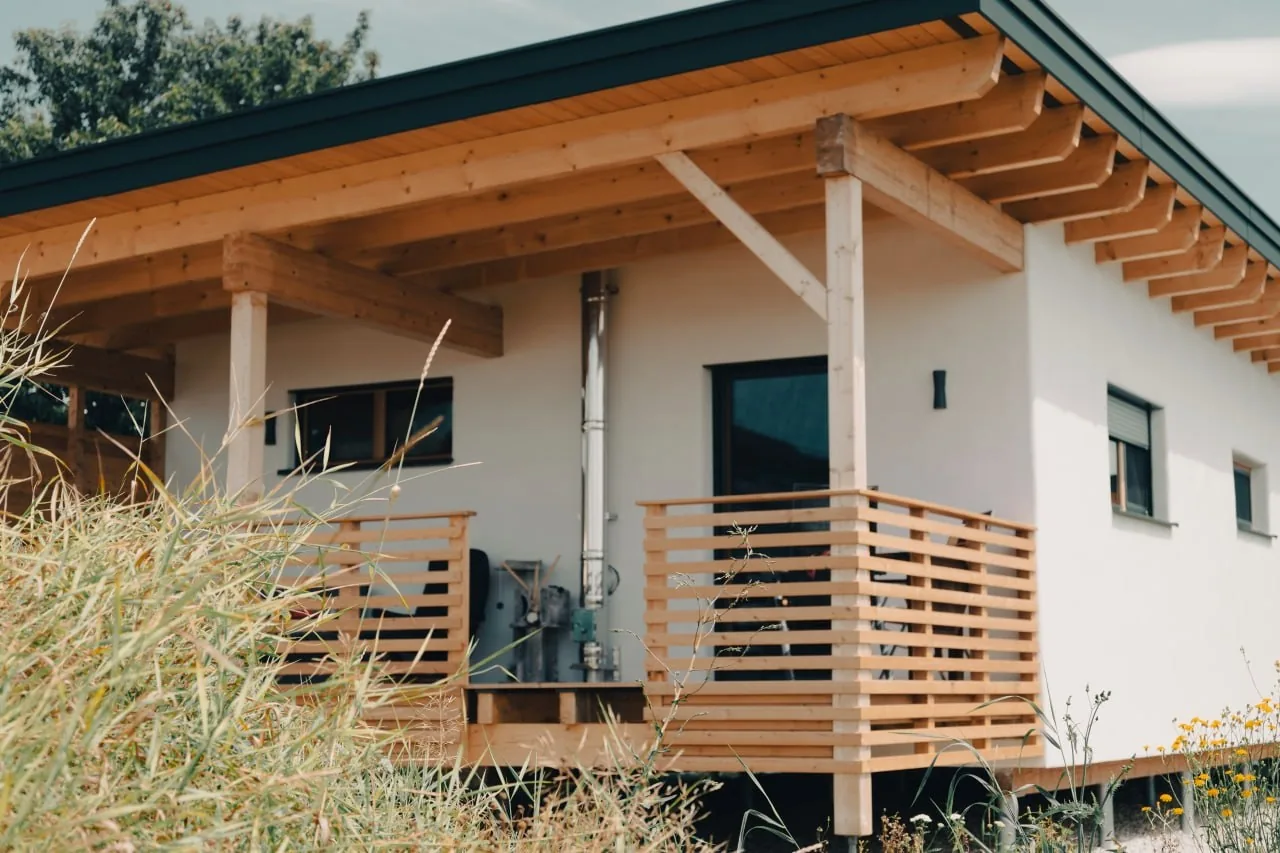Tinyhaus Martina: Überdachte Holzterrasse mit Lattengeländer, dahinter die weiße Putzfassade
